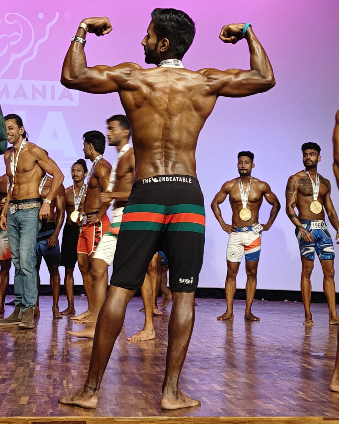 MuscleMania December 2024 rear double biceps pose on stage